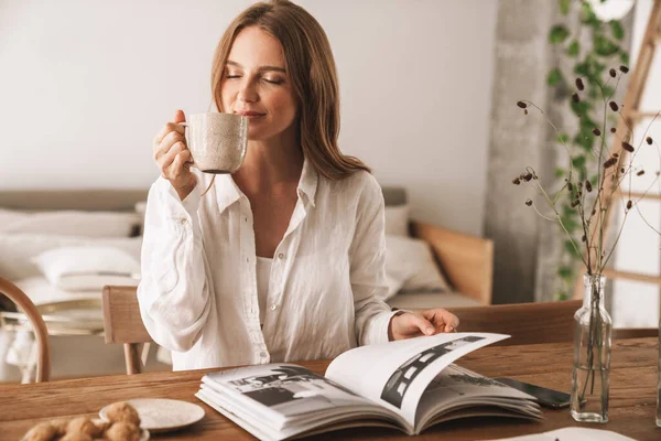 Woman sit indoors in office reading magazine drinking coffee. — Stock Photo, Image