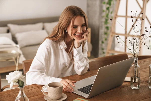 Cheerful cute beautiful business woman sit indoors in office using laptop computer listening music with earphones. — Stock Photo, Image