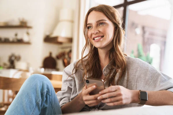 Lächelnd fröhlich schöne rothaarige Frau zu Hause mit dem Handy. — Stockfoto