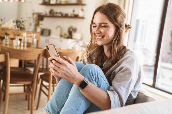 Smiling cheerful beautiful redhead woman at home using mobile phone. — Stock Photo, Image