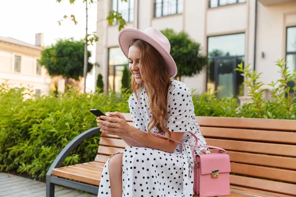 Piros hajú nő ül egy padon beszélgetni mobiltelefonnal. — Stock Fotó