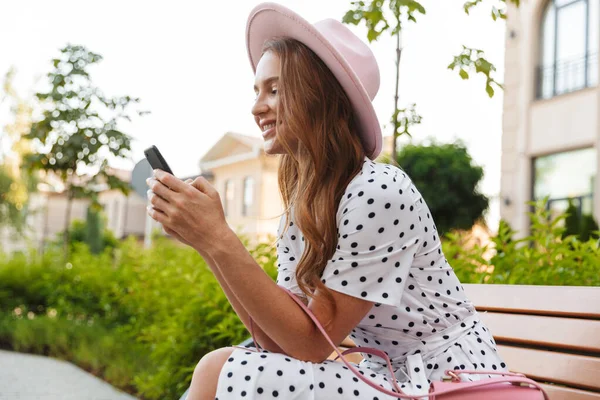 Mulher ruiva senta-se em um banco conversando por telefone celular . — Fotografia de Stock