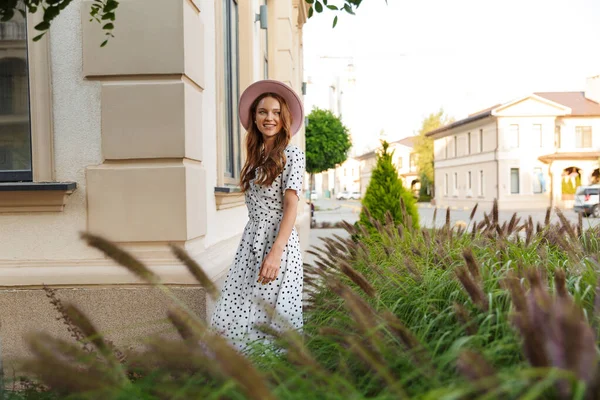 Redhead woman walking by street outdoors in dress and hat. — Stock Photo, Image