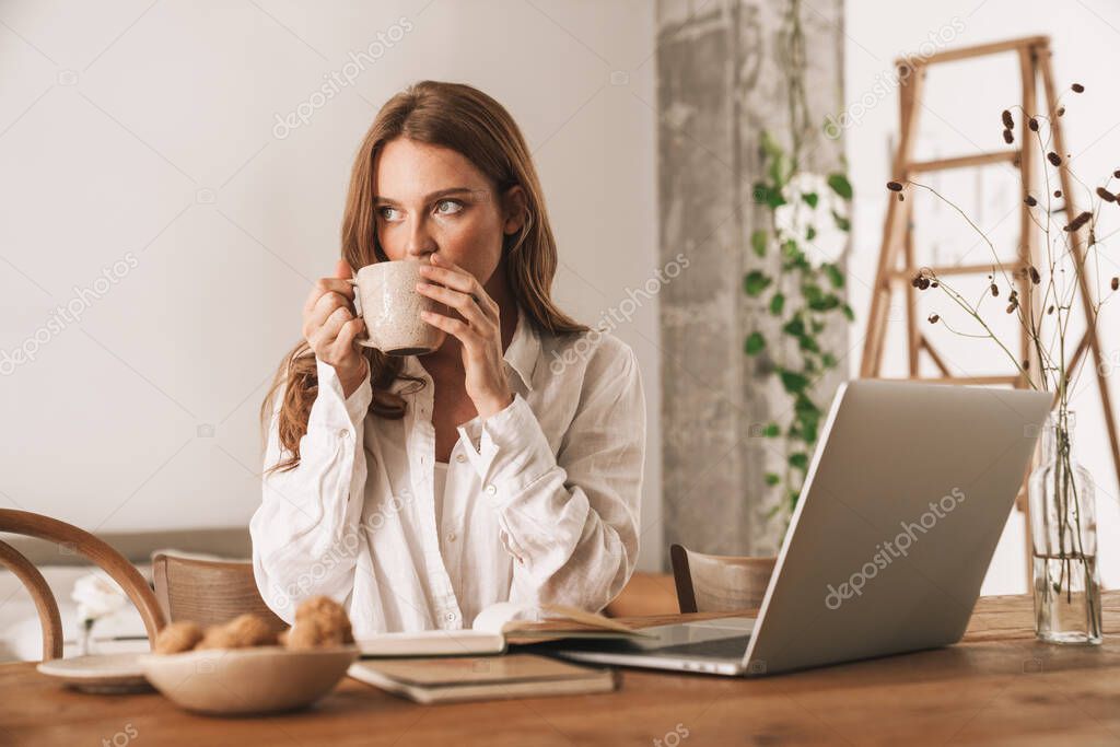 Redhead business woman sit indoors drinking coffee.