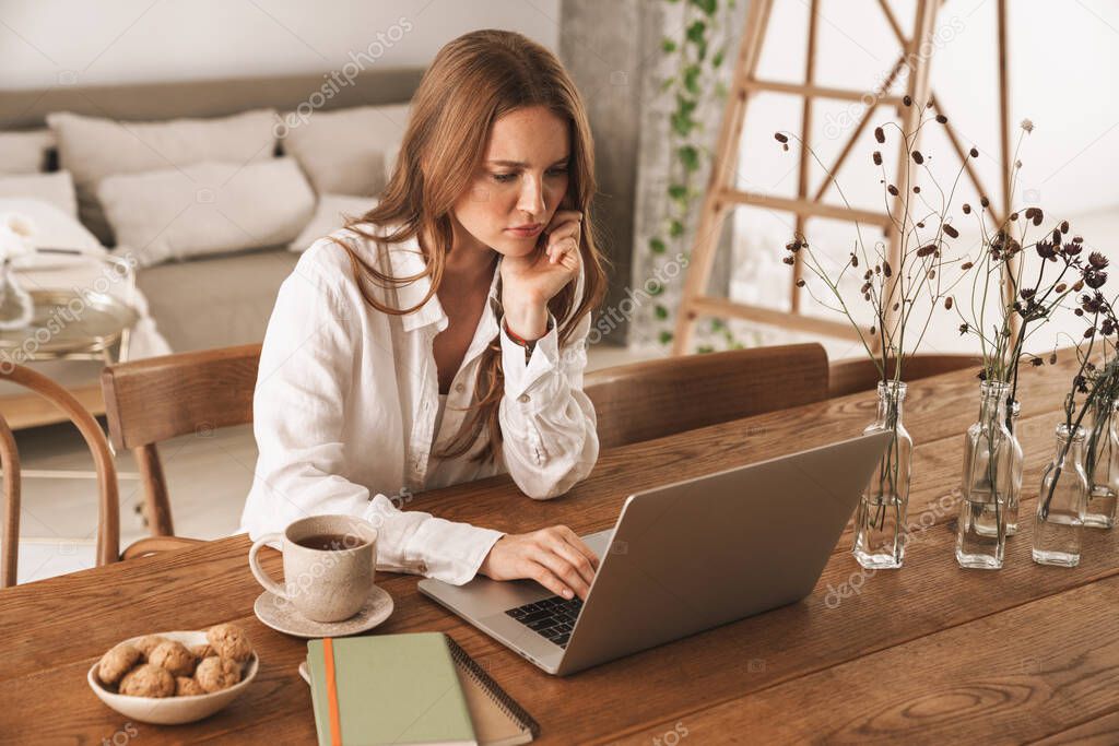 Displeased ginger business woman using laptop computer.