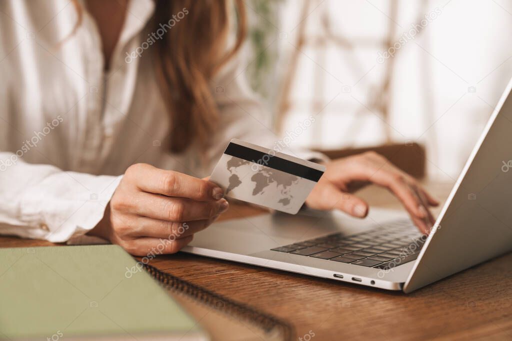Woman sit indoors in office using laptop computer holding credit card.