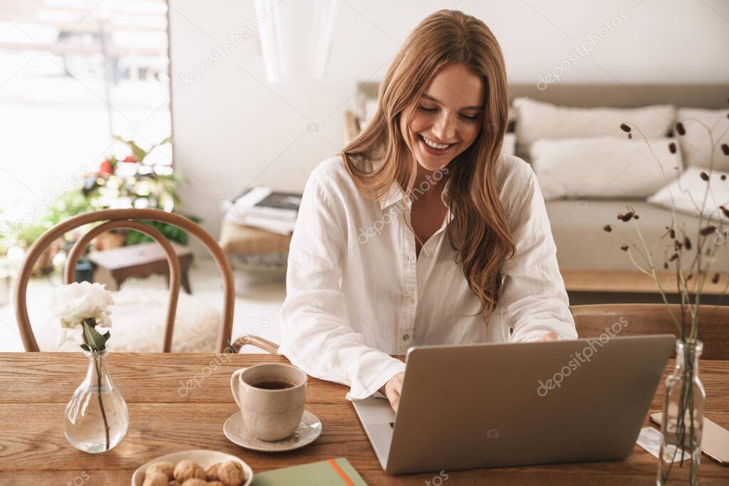 Happy positive cute beautiful business woman sit indoors in office using laptop computer.