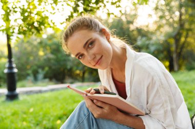 Güzel bir genç kız, sıradan giyinmiş, bankta oturuyor.