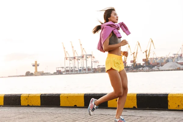 Imagen de mujer asiática en ropa deportiva corriendo contra el mar por — Foto de Stock