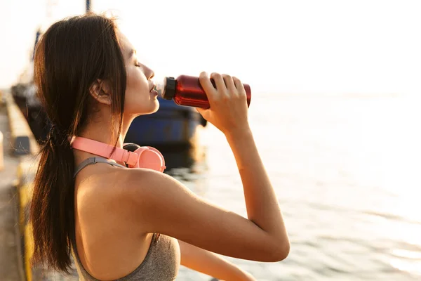 헤드폰을 끼고 물을 마시는 운동 선수 아시아 여성의 모습 — 스톡 사진