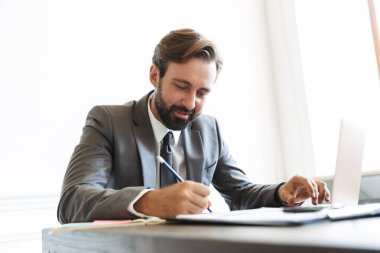 Not yazarken laptopta çalışan kendinden emin iş adamının resmi