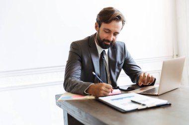 Not yazarken laptopta çalışan tıraşsız odaklı iş adamının resmi