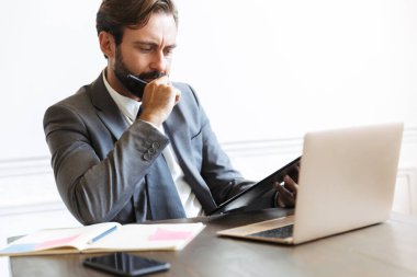 Ofiste dizüstü bilgisayar başında çalışırken kafası karışık iş adamının dokümanları okuması