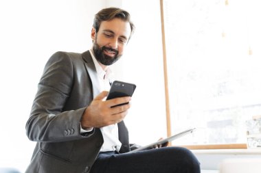 Ofiste çalışırken cep telefonuyla yazı yazan ve panoyu tutan memnun iş adamının resmi