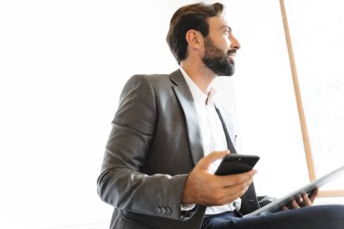 Ofiste çalışırken cep telefonu kullanan ve pano tutan sakallı bir iş adamı resmi