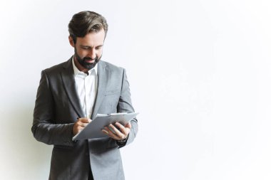 Yakışıklı, başarılı bir iş adamının elinde pano tutarken ve ofiste çalışırken notlar yazarken görüntüsü