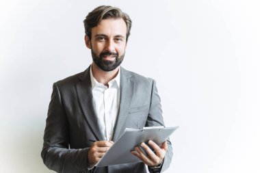 Görüntü: Akıllı, kendine güvenen iş adamı elinde bir pano tutarken ve ofiste çalışırken notlar yazarken.