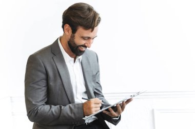 Ofiste çalışırken sakallı, gülen bir işadamının pano tutarken ve notlar yazarken görüntüsü