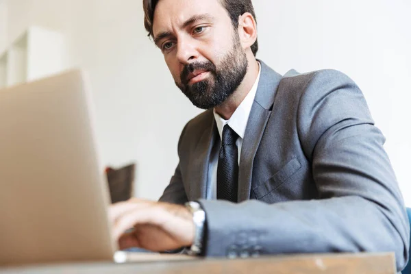 Uomo d'affari barbuto concentrato seduto in ufficio utilizzando computer portatile che lavora al chiuso . — Foto Stock