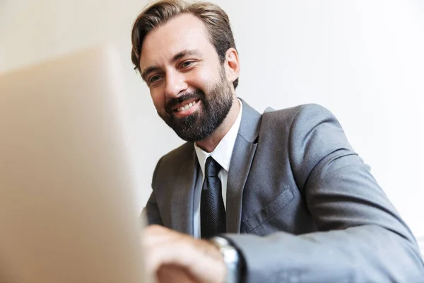 Guapo joven hombre de negocios positivo sentado en la oficina utilizando ordenador portátil de trabajo en interiores . —  Fotos de Stock