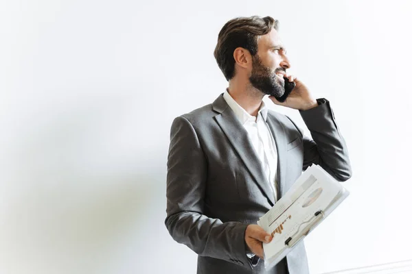 Image of handsome caucasian businessman talking on cellphone and holding clipboard while working in office — Stock Photo, Image