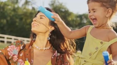 Mutlu Hintli kadın dışarıda balon üfleyicisiyle oynarken neşeli kızıyla eğleniyor.