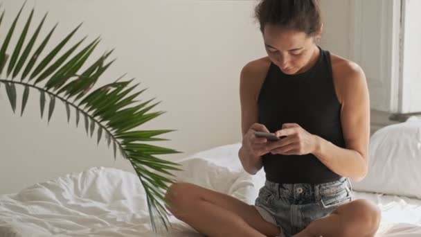 Sorrindo Muito Asiático Mulher Escrevendo Mensagem Smartphone Enquanto Sentado Cama — Vídeo de Stock