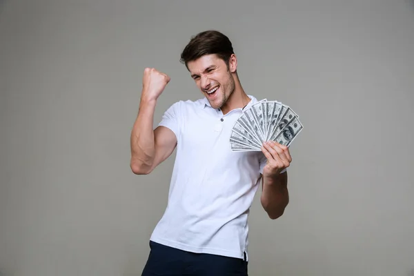 Эмоциональный молодой человек делает жест победителя держа деньги . — стоковое фото