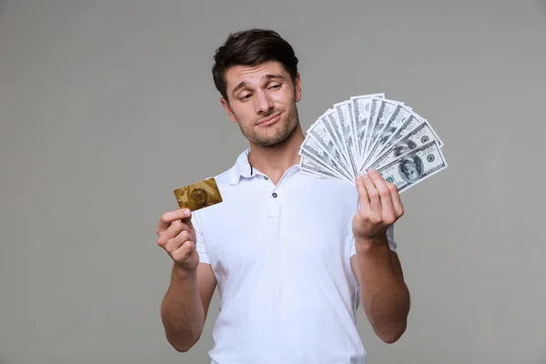 Thinking man holding money and debit card. — Stock Photo, Image