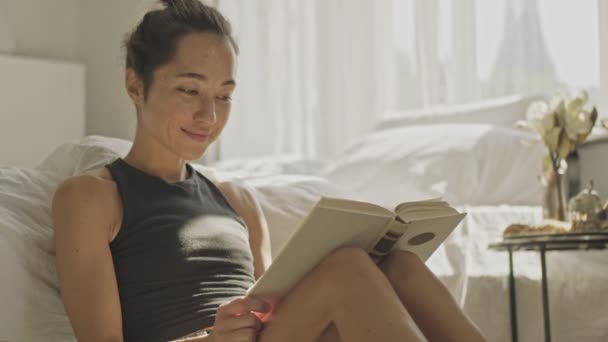自宅の床に座って本を読んでいるかなりアジアの女性を喜ばせました — ストック動画