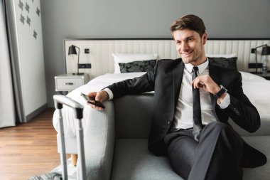 Kanepede oturan akıllı telefonlu ve gülümseyen genç bir adam.