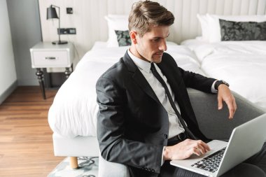 Kanepede dizüstü bilgisayarla oturan ciddi bir genç resmi. 