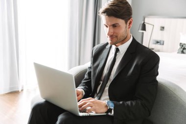 Kanepede dizüstü bilgisayarla oturan kendinden emin bir genç resmi.