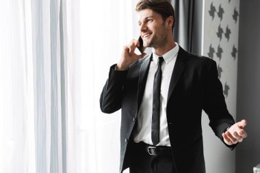 Evdeki iş adamı büyük pencerenin yanında cep telefonuyla konuşuyor..