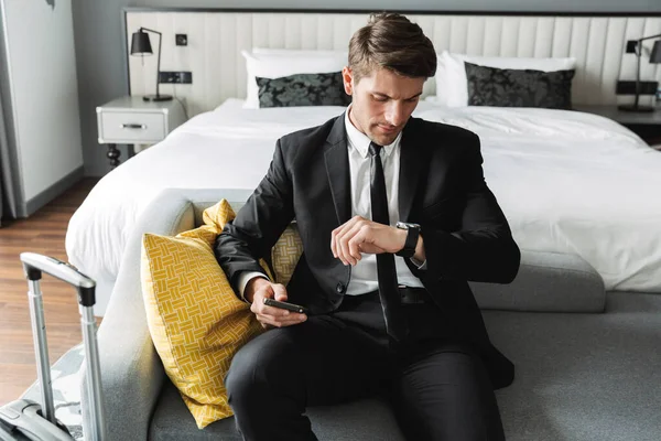 Image of handsome young man sitting on sofa with smartphone and — Stock Photo, Image