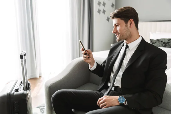 Image of happy young man sitting on sofa with smartphone and sui — Stock Photo, Image