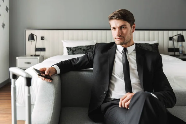 Image of caucasian young man sitting on sofa with smartphone and — Stock Photo, Image