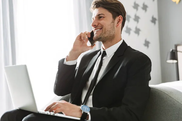 幸せな若い笑顔ビジネスマン屋内で自宅でノートパソコンを使用して話す携帯電話. — ストック写真