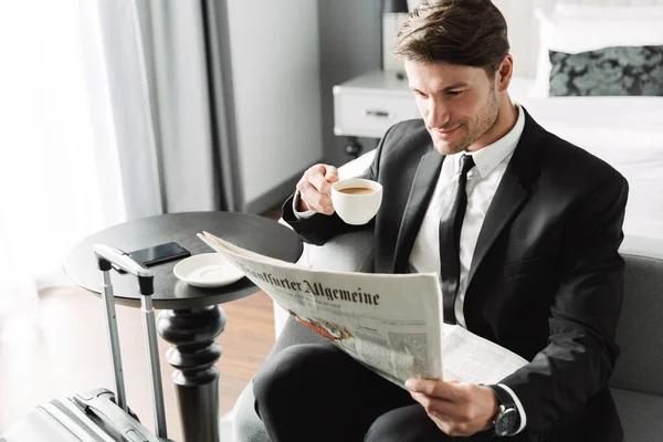 Concentrated businessman indoors at home reading newspaper drinking coffee. — Stock Photo, Image