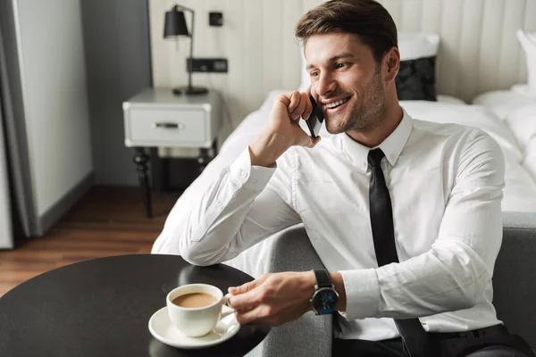 Image of businesslike young man talking on smartphone and drinki — Stock Photo, Image
