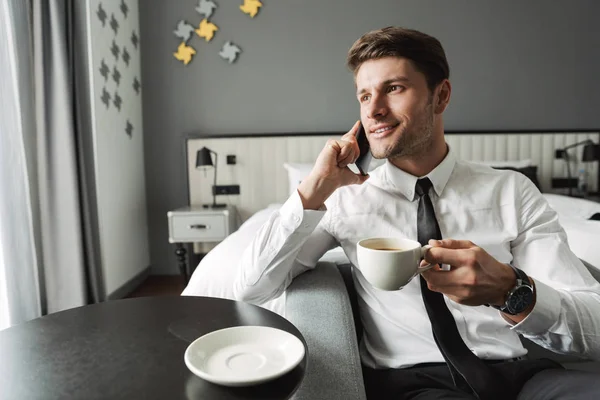 Image of attractive young man talking on smartphone and drinking — Stock Photo, Image