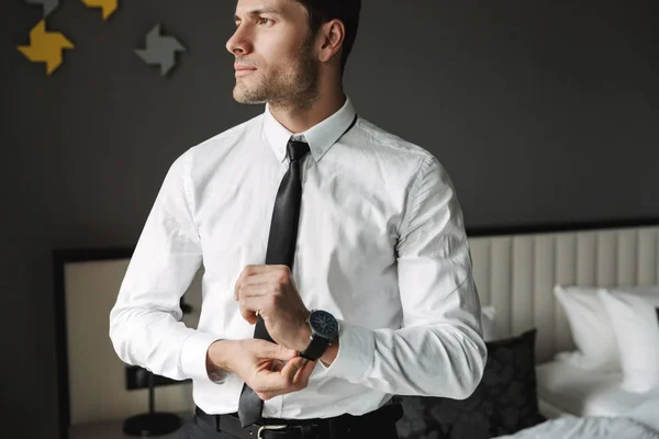 Bild av självsäker ung man som tar av sig sitt armbandsur på hotellet — Stockfoto