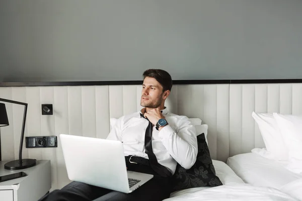 Image of handsome young man lying on bed with laptop computer in — Stock Photo, Image