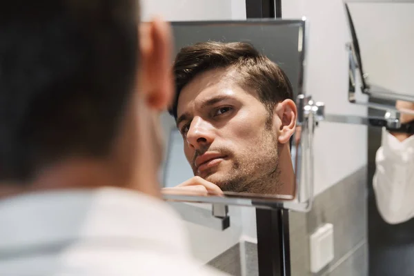 Imagen de primer plano del hombre sin afeitar mirando el espejo en el baño en h — Foto de Stock