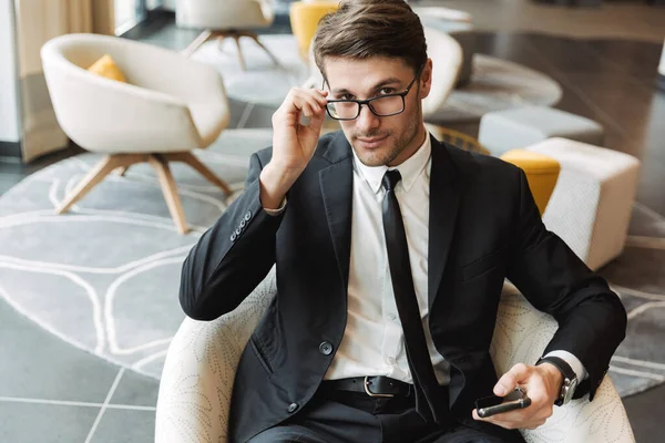 Photo of successful young man sitting in hotel hall with smartph — Stock Photo, Image