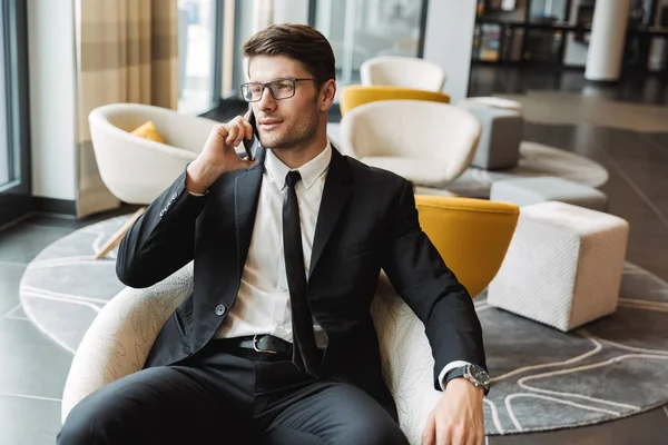 Photo of businesslike young man sitting in hotel hall with smart — Stock Photo, Image