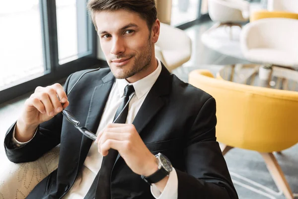 Photo of successful young man holding eyeglasses in hotel hall d — Stock Photo, Image