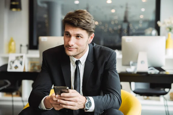 Portrait of brunette young businessman sitting on armchair with — Stock Photo, Image