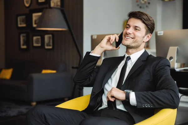 Portret van vrolijke jonge zakenman zittend op fauteuil met sm — Stockfoto