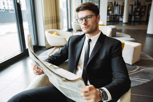 Portrait of handsome young businessman sitting on armchair and r — Stock Photo, Image